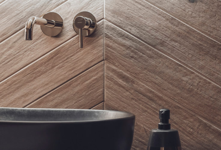 tapeta w liście, czarna szafka umywalkowa, czarna umywalka, ciemna łazienka, złote dodatki, luksusowa łazienka, płytki w jodełkę, podświetlane lustro alfaram